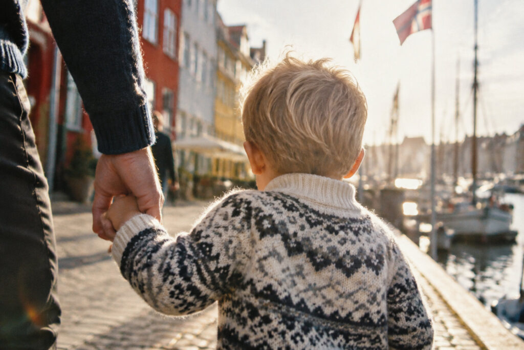 Un petit garçon blond en pull norvégien tient la main de son père le long d'un quai au Danemark.