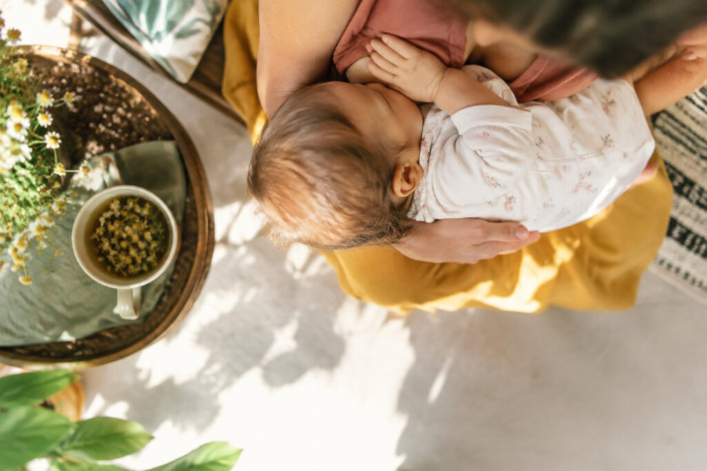 Une mère allaite son bébé dans un environnement chaleureux avec une tisane aux fleurs posée sur une table à proximité.